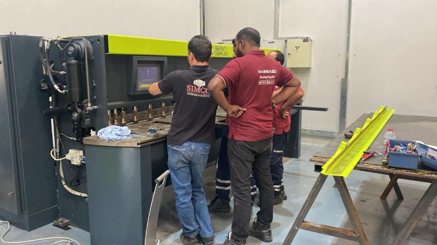 فريق شركة مصاعد أثناء إعداد ماكينة القص CNC التي تقطع الصفائح المعدنية لألواح التكسية